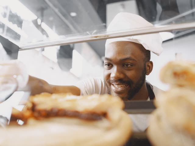 Boulanger souriant, dans une boulangerie-pâtisserie moderne, prêt à recevoir sa clientèle.
